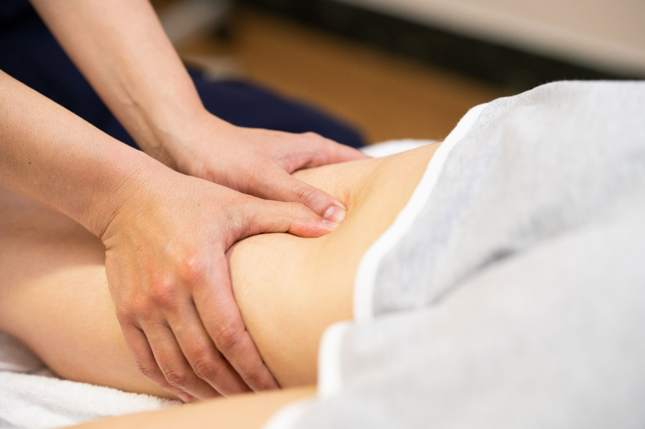 A masseur performs a lymphatic massage treatment on the patient's thigh, stimulating lymphatic circulation with gentle, targeted movements.